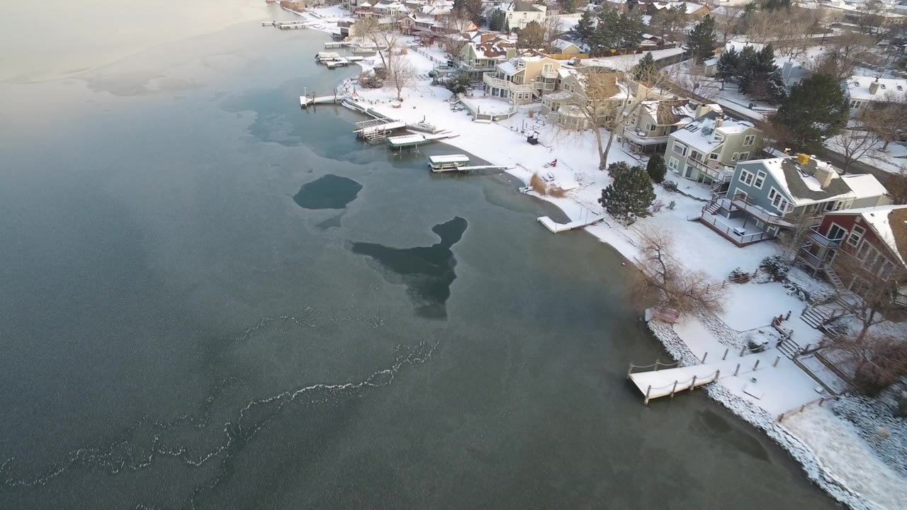 Snowy lakeshore homes beside docks and partially frozen water.