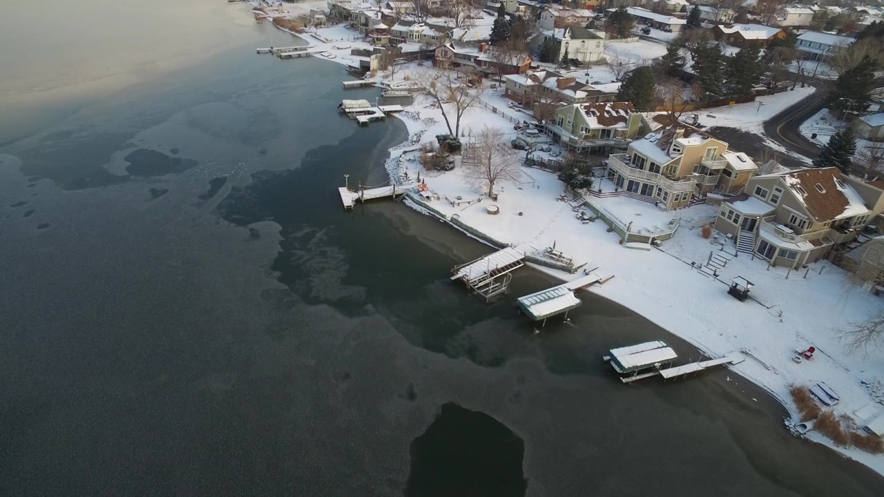 Snowy lakeside homes and docks beside dark partially frozen water.