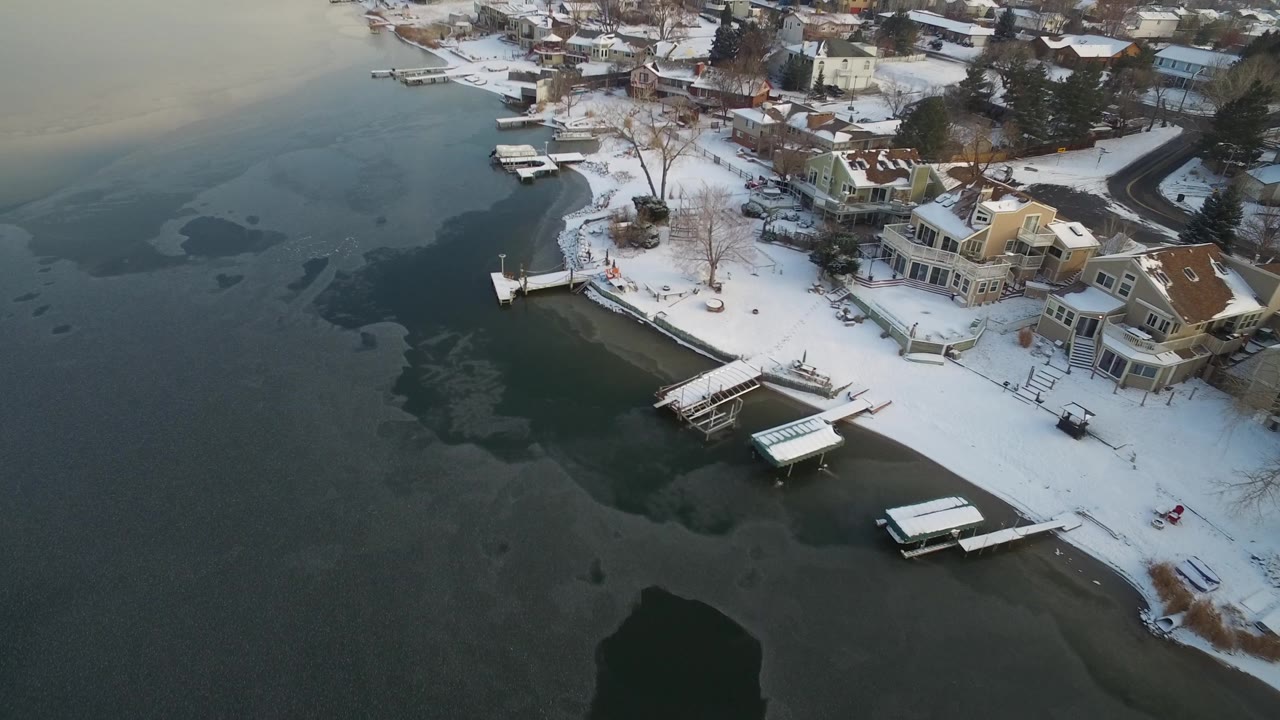 Oblique aerial over Hidden Lake, Colorado with waterfront houses at right, docks along the snowy bank, broad dark lake ice patterns, and no visible people.