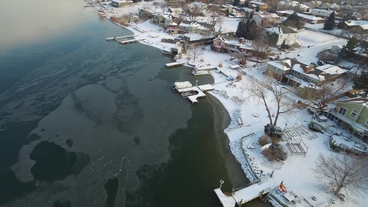 Snowy lakeside homes beside dark water and thin ice