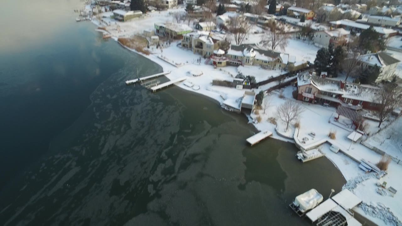 Snowy residential shoreline curves along a partly frozen lake.