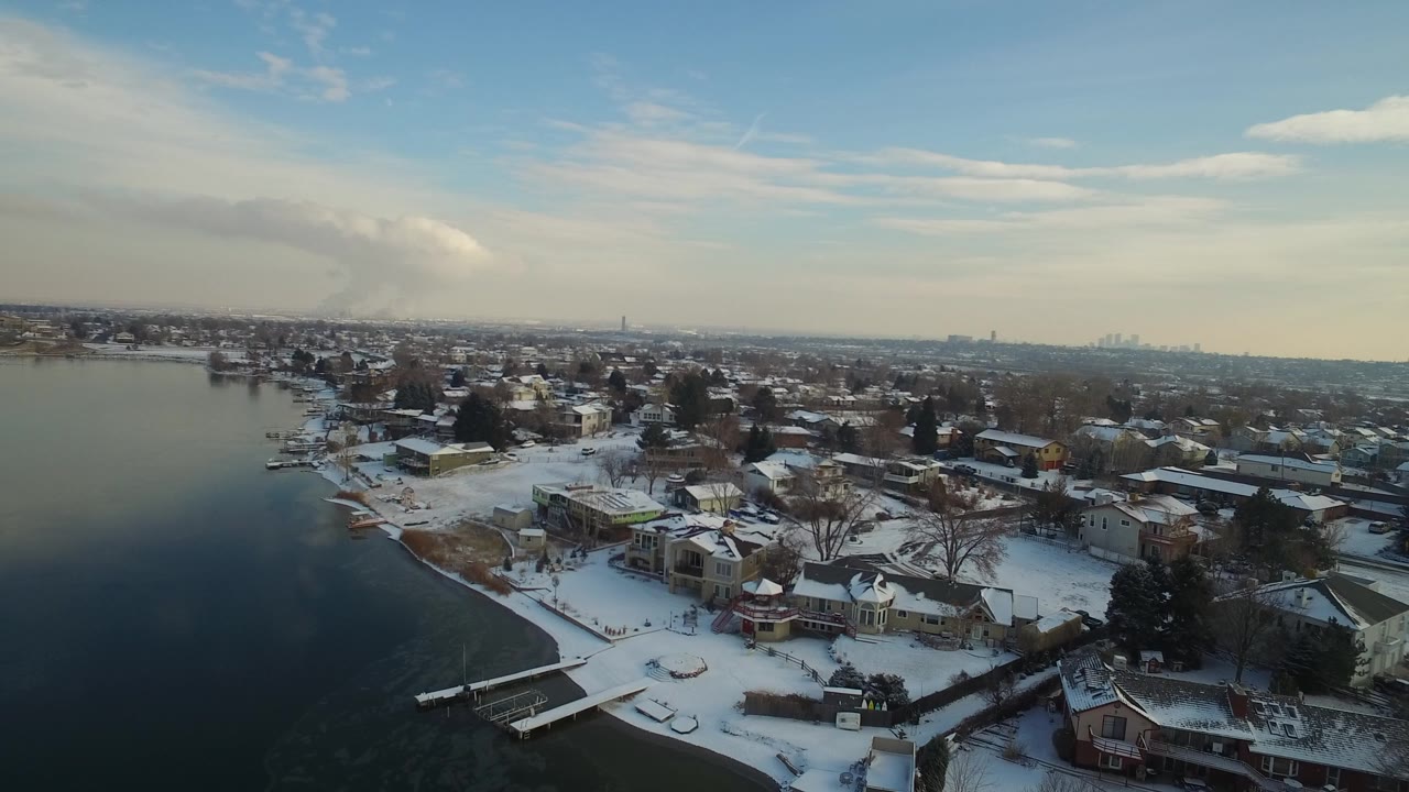 Snowy lakeside neighborhood seen from above beside dark water.