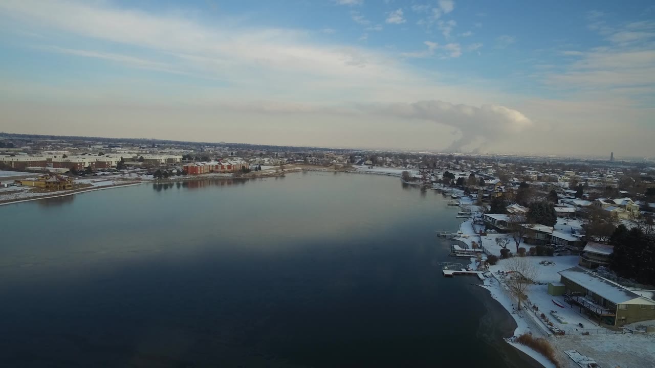 Hidden Lake, Colorado appears from an elevated angle with open water filling the foreground, snow along the right shoreline, small docks, distant buildings, and no visible people.