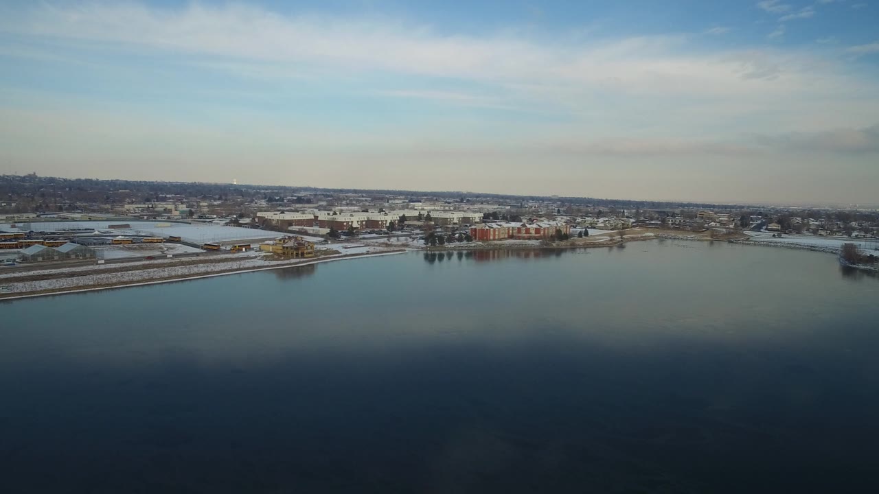 Aerial view across a broad lake toward a snowy shoreline and town.