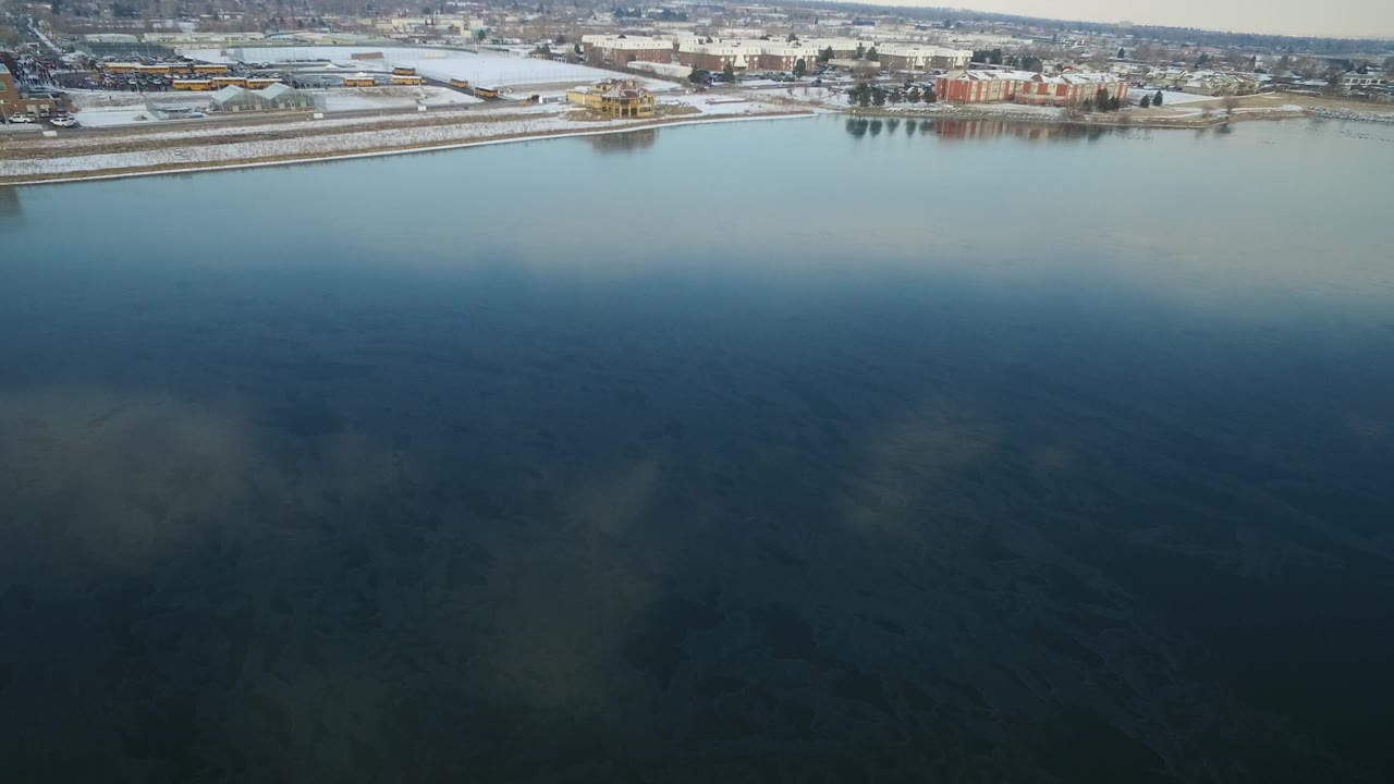 Aerial view over a lake toward a snowy shoreline and town buildings.
