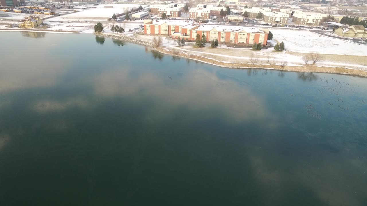 Snowy lakeside building seen from above across dark blue-green water.