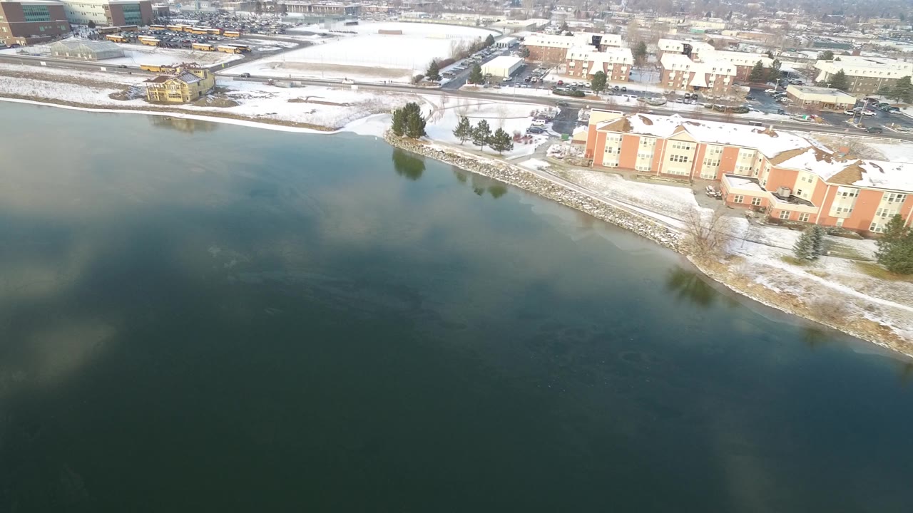 Aerial view of dark lake water beside a snowy residential shoreline.