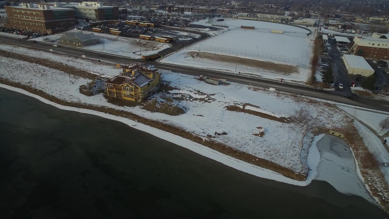 Snowy lakeside property with a house, road, and distant buses.