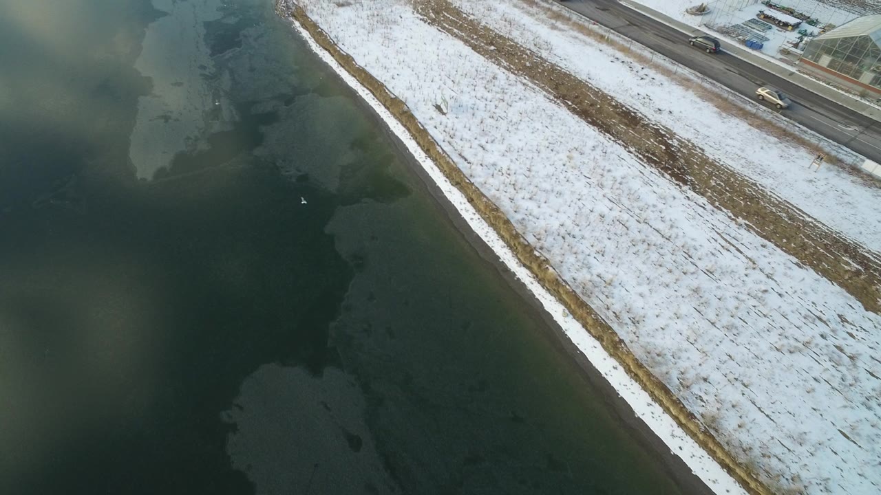 Snowy shoreline beside dark green water and a road at the top of frame.