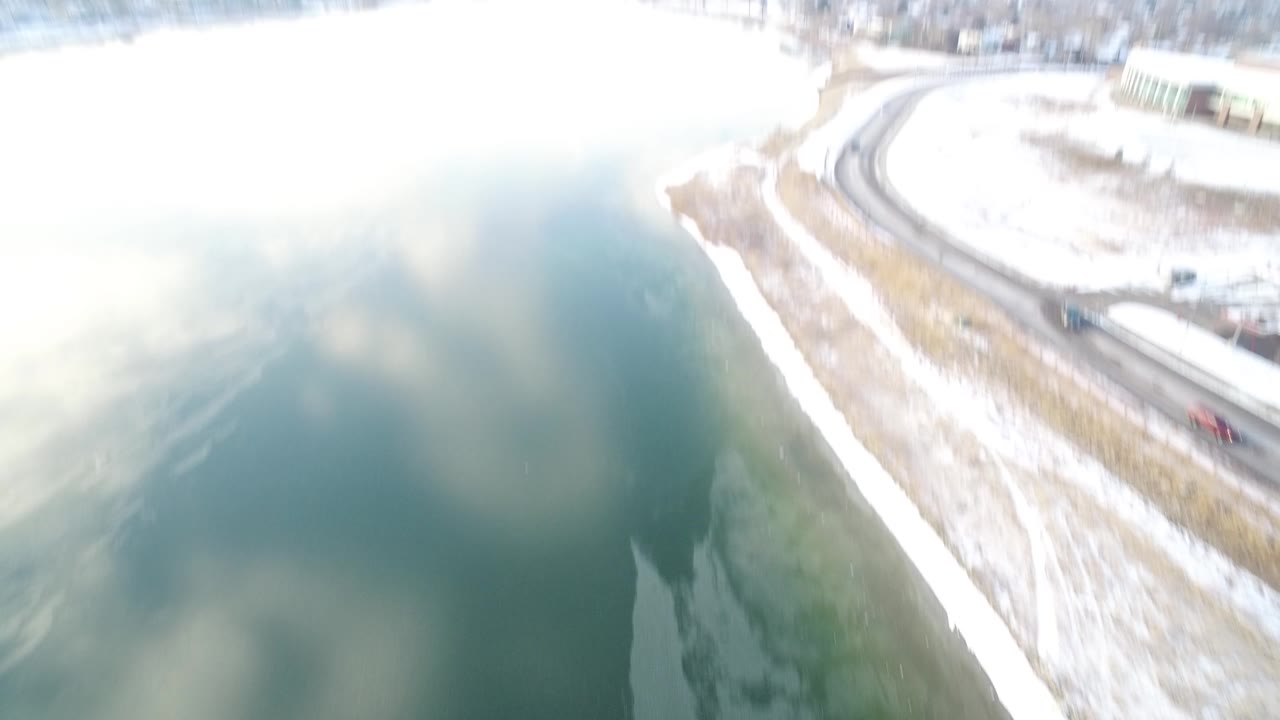 Early aerial frame over Hidden Lake, Colorado showing bright glare on the water, a snowy shoreline edge, and no visible people.