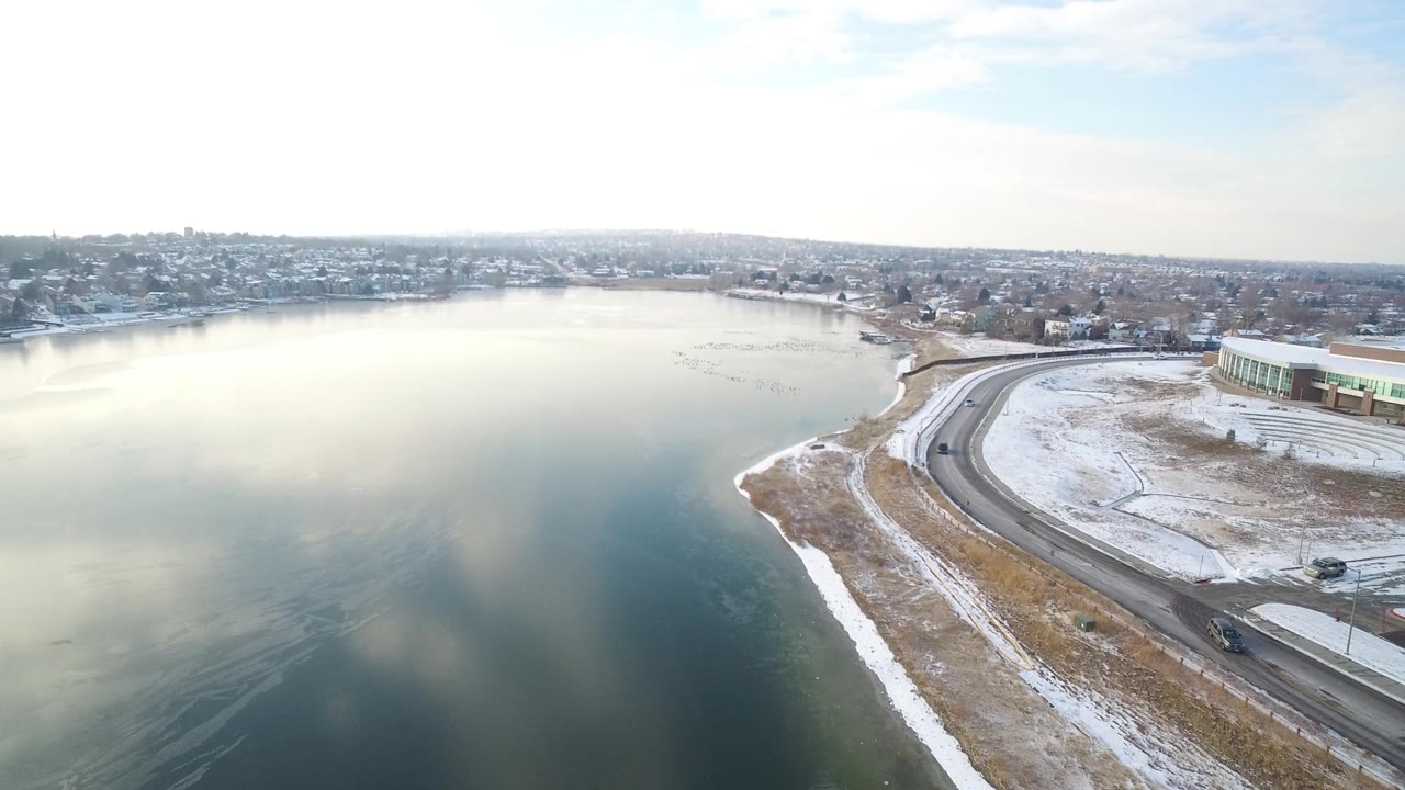 Wide aerial view of lake, neighborhood, road, and large building