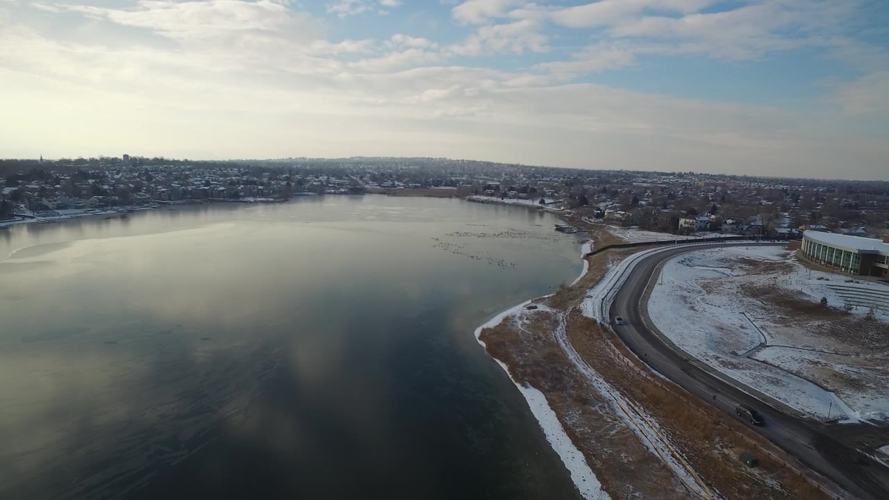 Drone-height view of a lake with a road tracing the snowy shore.