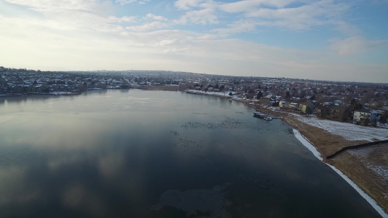 Aerial view of a lake beside a residential shoreline with snow patches.