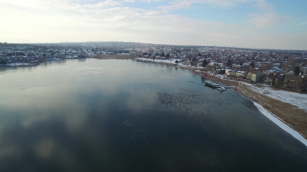 Aerial view of a lake beside snowy shoreline and homes.