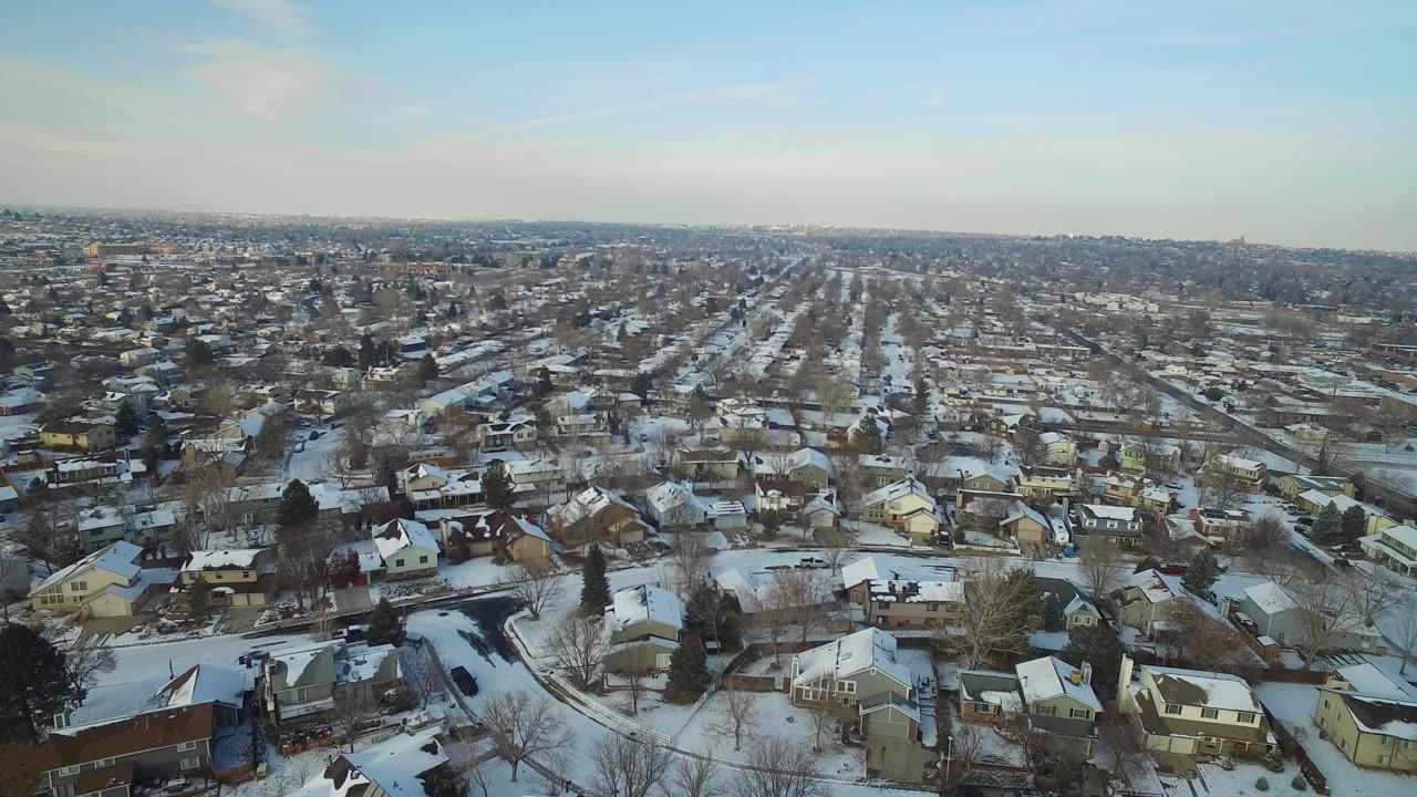Wide aerial frame over Hidden Lake, Colorado showing snow-covered residential blocks, bare trees, distant horizon, and no visible people.