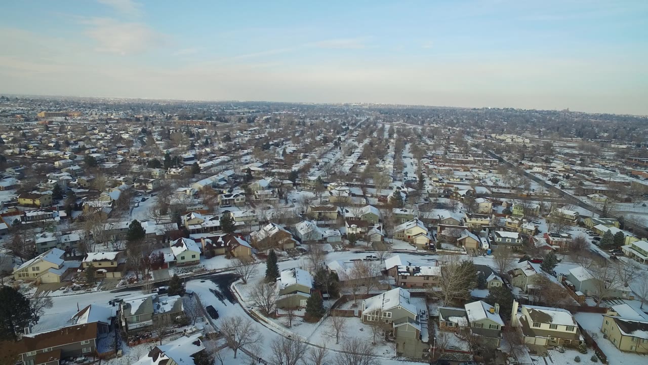 Aerial view over Hidden Lake, Colorado with repeating rows of snowy rooftops, leafless trees, neighborhood streets, and no visible people.