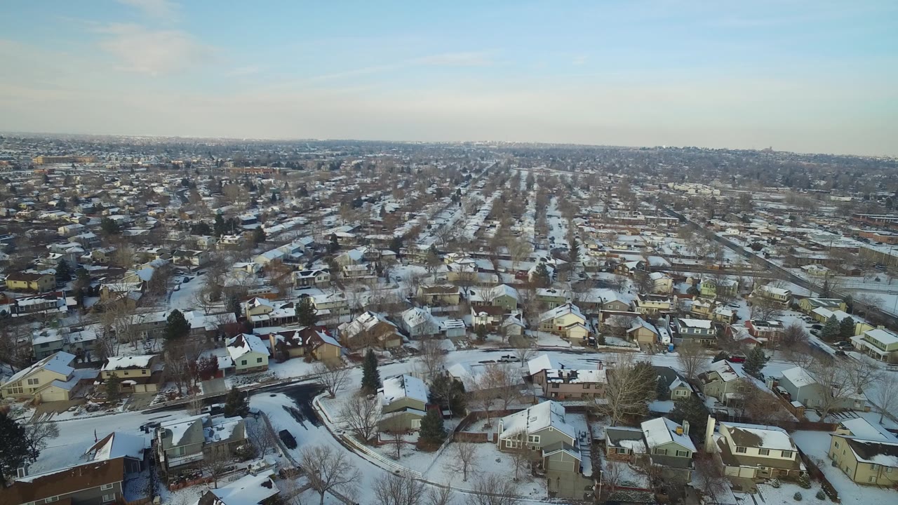 High aerial neighborhood view with snow on houses, yards, and roads.