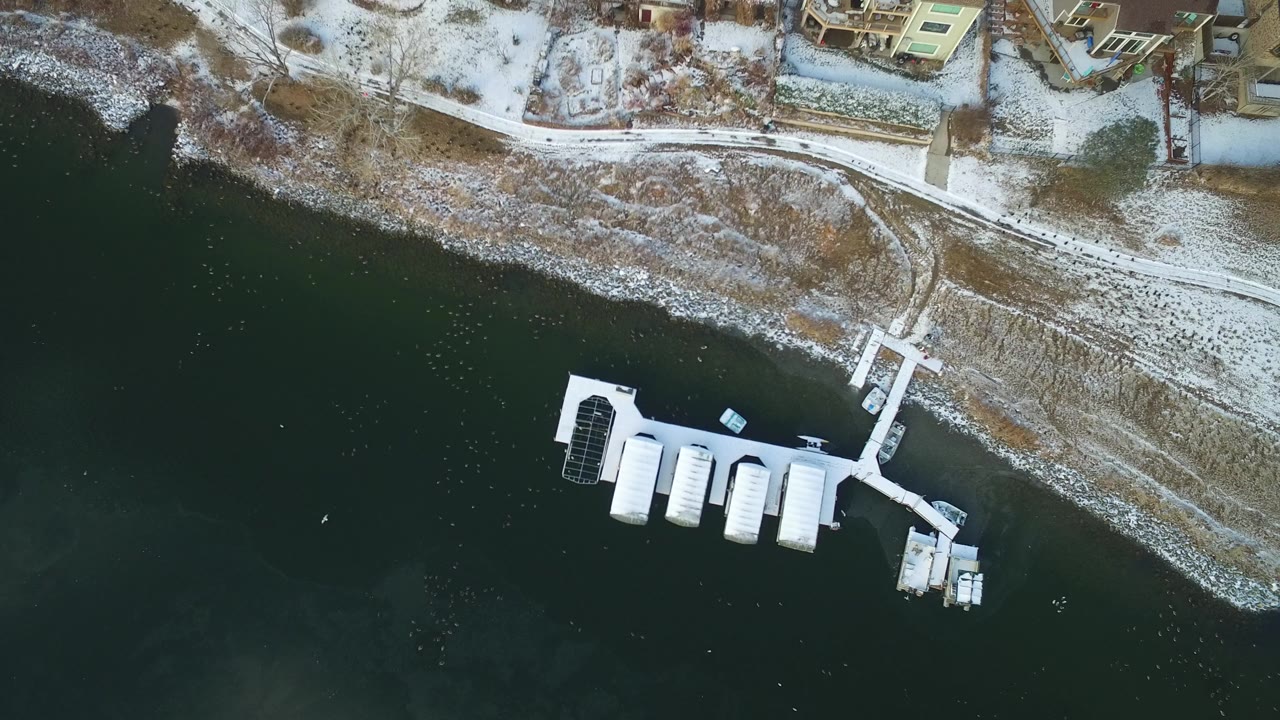 Overhead view of a snowy lakeshore with a dock and covered boat slips.