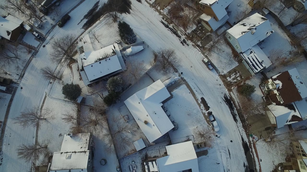 Aerial frame over Hidden Lake, Colorado homes, showing a pale curved road, white rooftops, winter yards, parked vehicles, and no visible people.