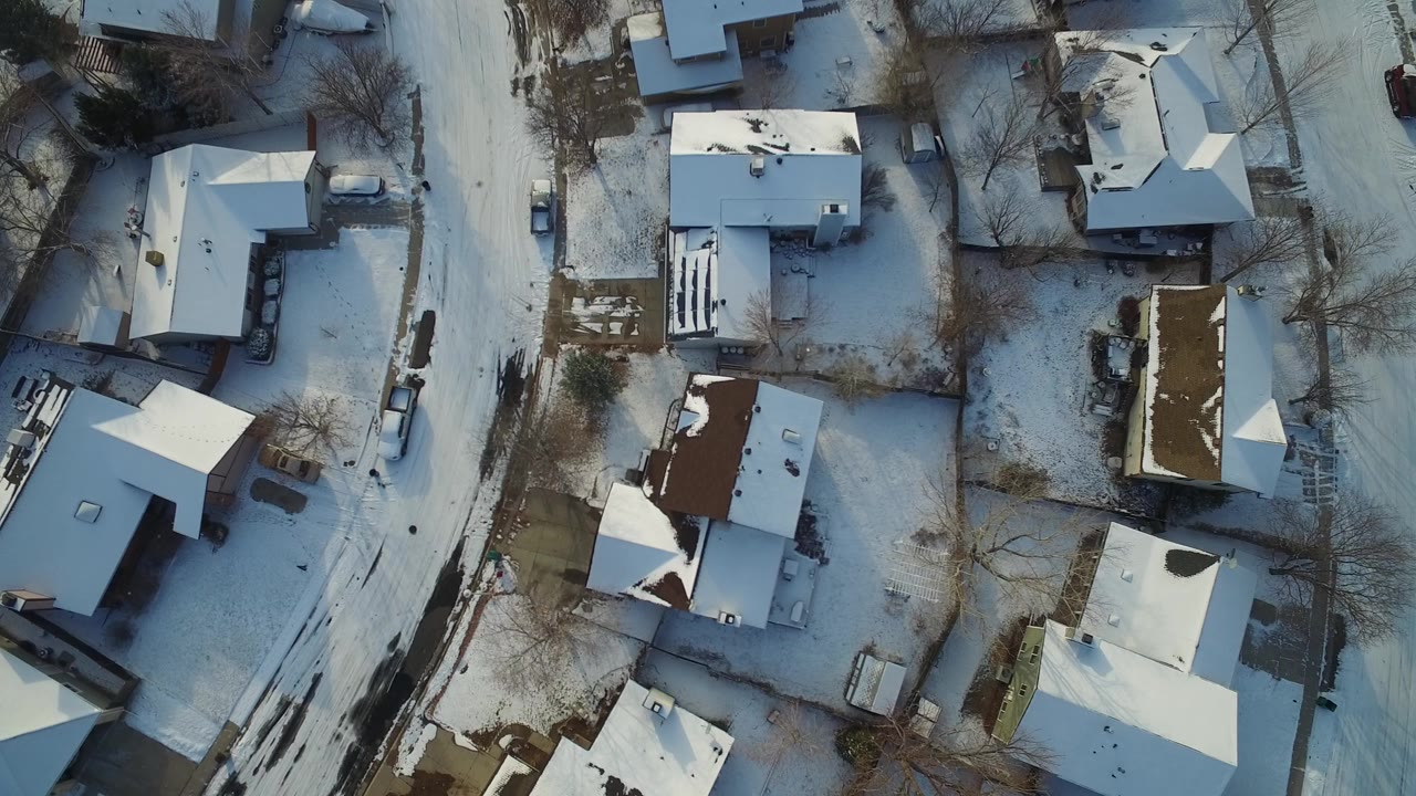 Overhead view of snow-covered houses and a curved residential street in Hidden Lake, Colorado, with bare trees, blue winter shadows, and no visible people.