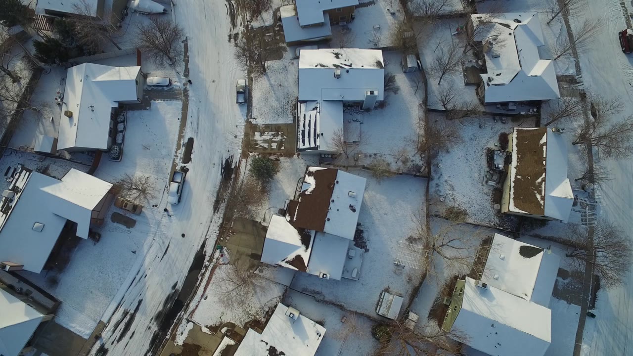 Top-down frame over Hidden Lake, Colorado homes, showing white roofs, small yards, leafless trees, and a snow-dusted road with no visible people.