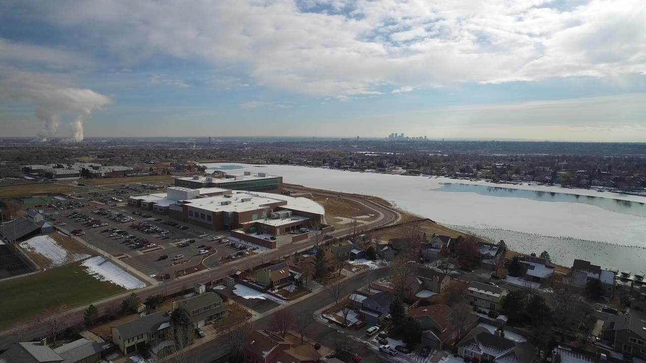 Aerial view of a lake, large building complex, homes, and distant skyline.
