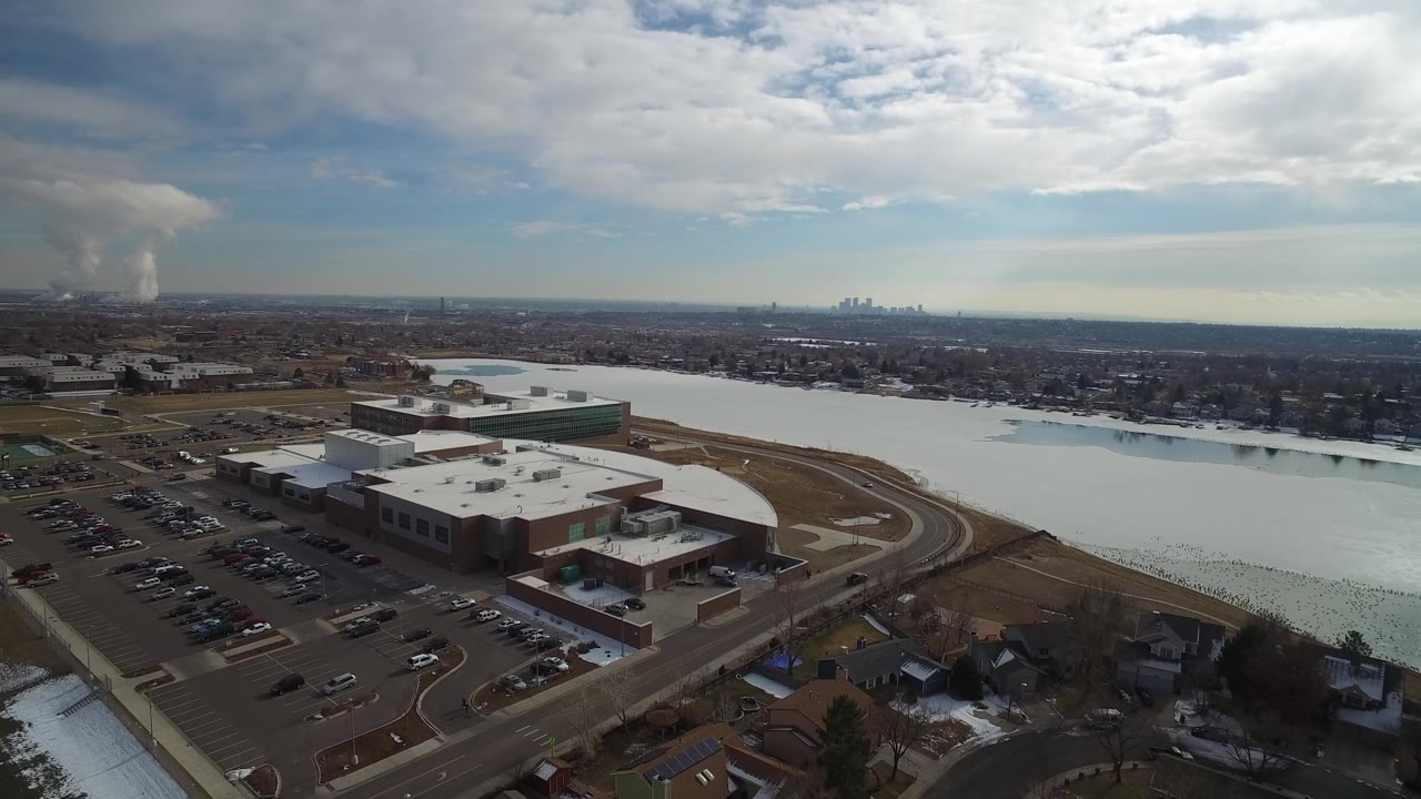 Aerial view of a large building beside a lake and parking lots.