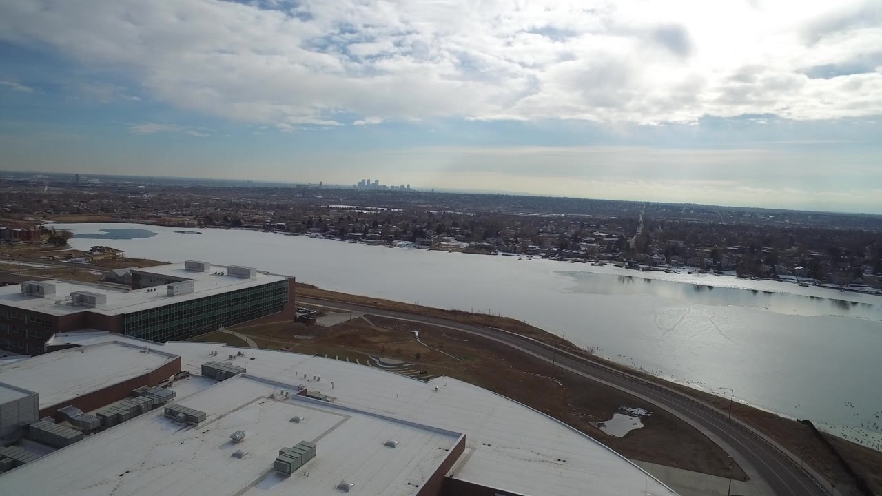 Aerial view over rooftops toward a broad water area and distant skyline.