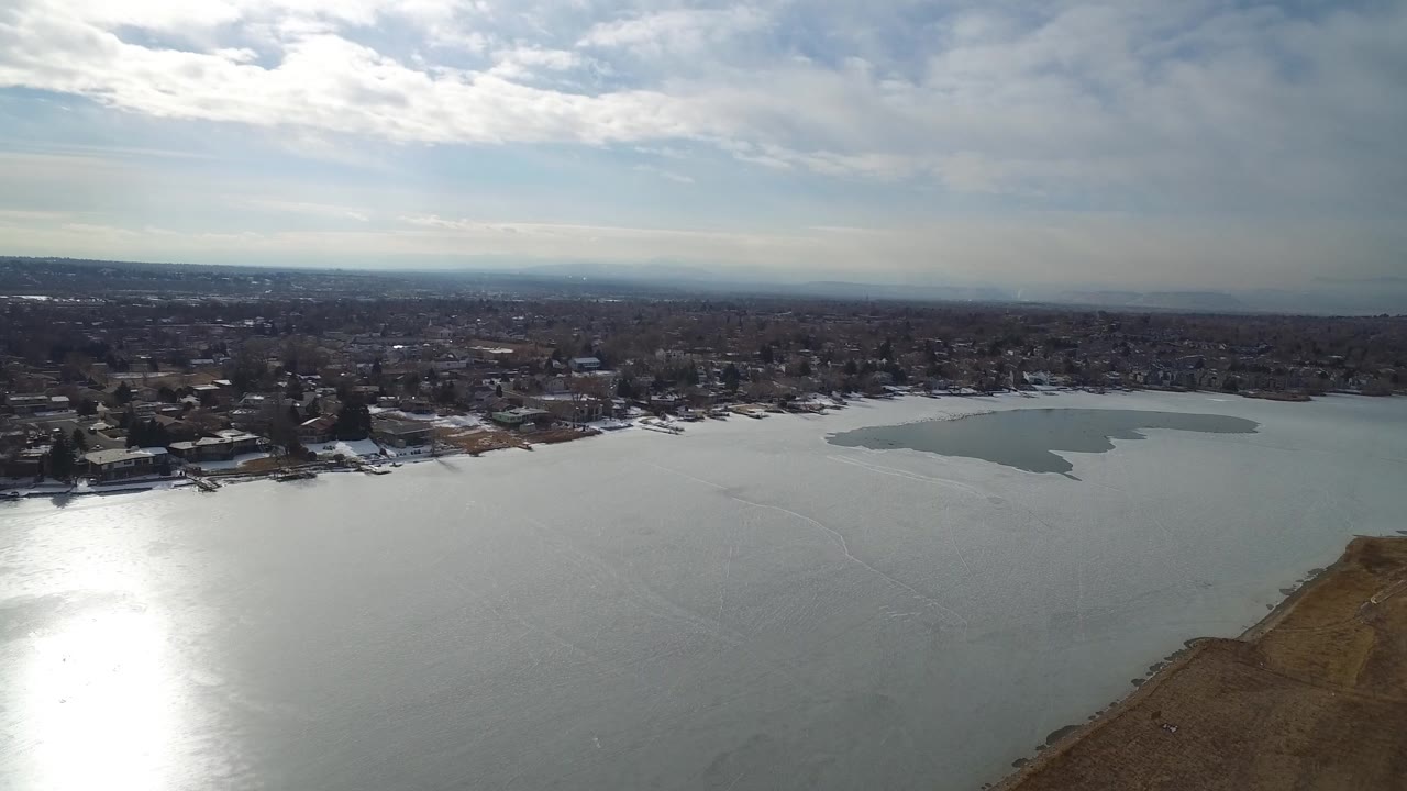 Lakefront aerial view with sun reflection and houses along shore.
