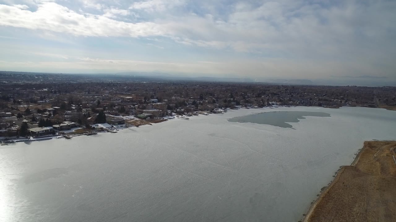 Aerial view over Hidden Lake, Colorado with gray-green water in the foreground, shoreline homes beyond it, a brown peninsula at right, and no visible people.