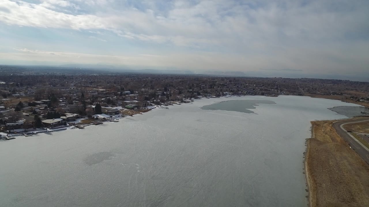 Frozen lake beside a residential shoreline under cloudy sky.