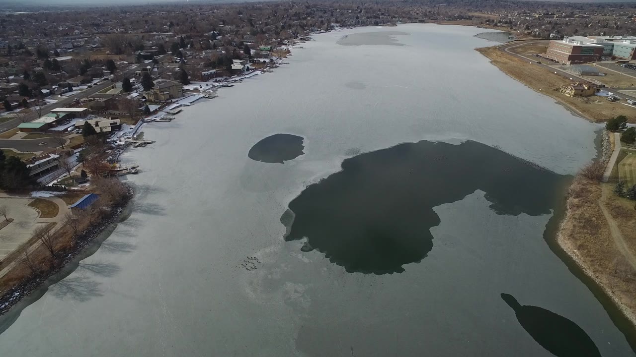 Aerial view of a partly frozen lake beside houses and commercial buildings.