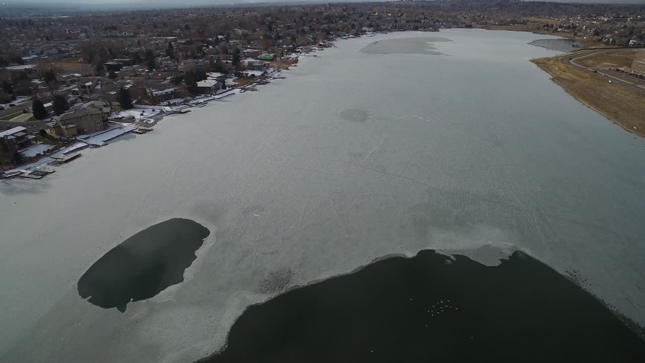 Frozen lake with open water patches and a town shoreline