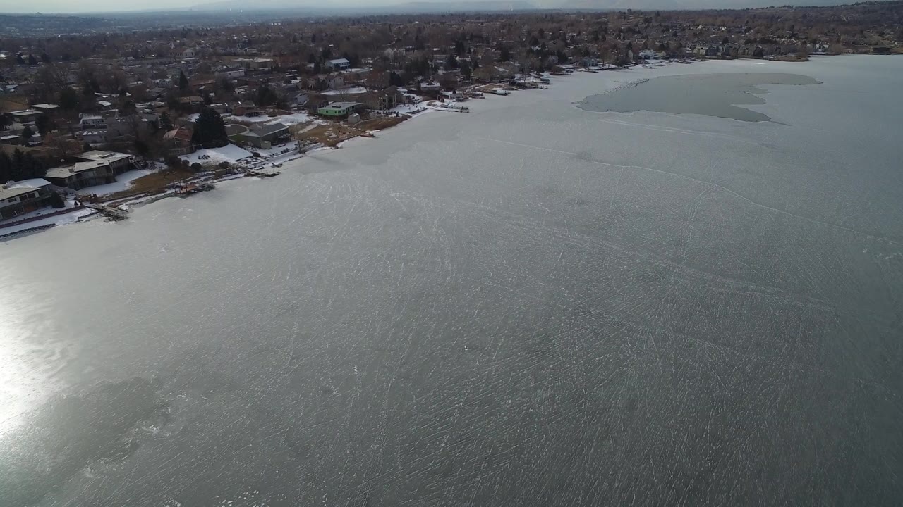 Wide aerial view of a frozen lake beside a residential shoreline.