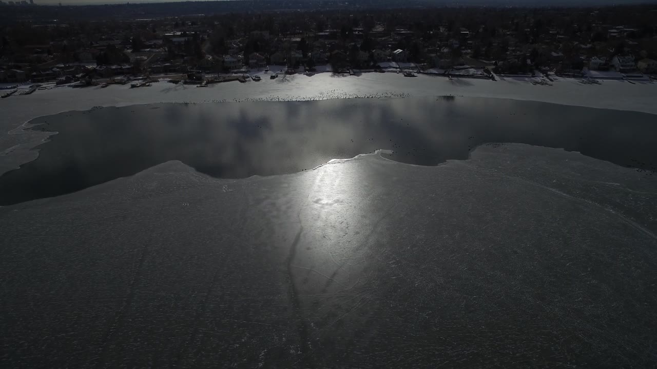 High aerial over a mostly frozen pond with a bright patch of glare on the ice.