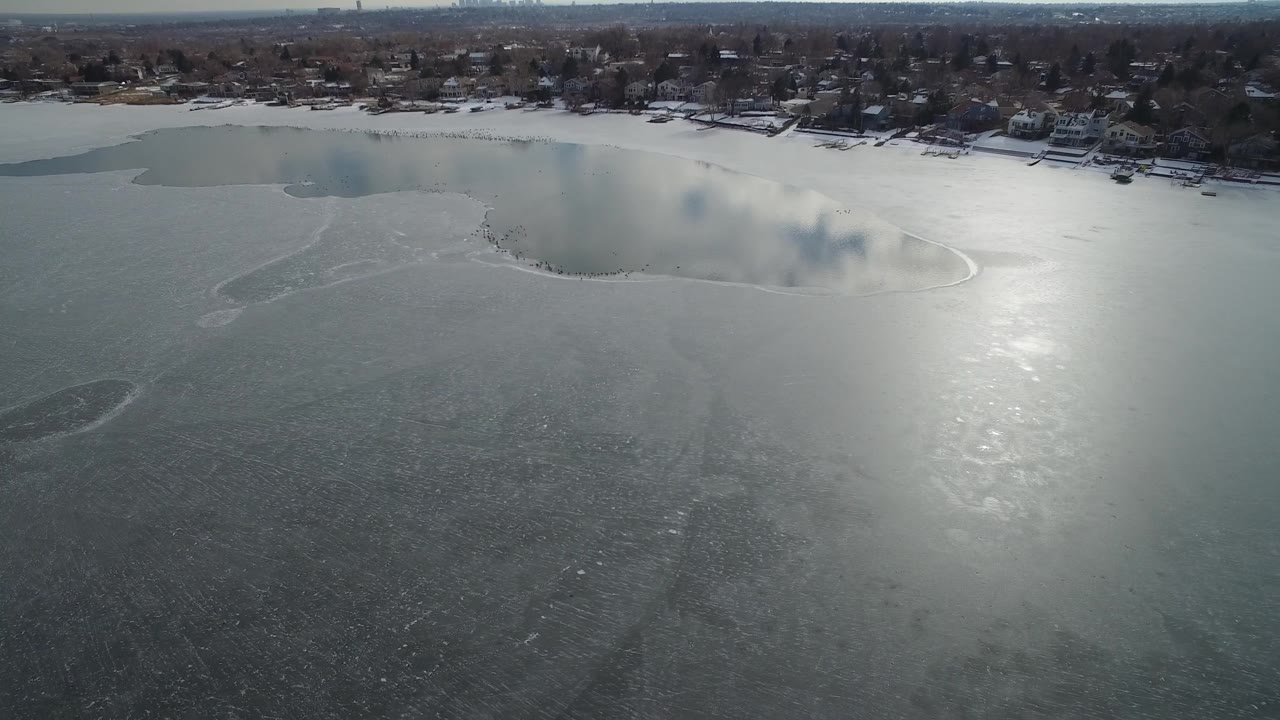 Frozen lake surface under bright glare with a residential shoreline across the top of frame.