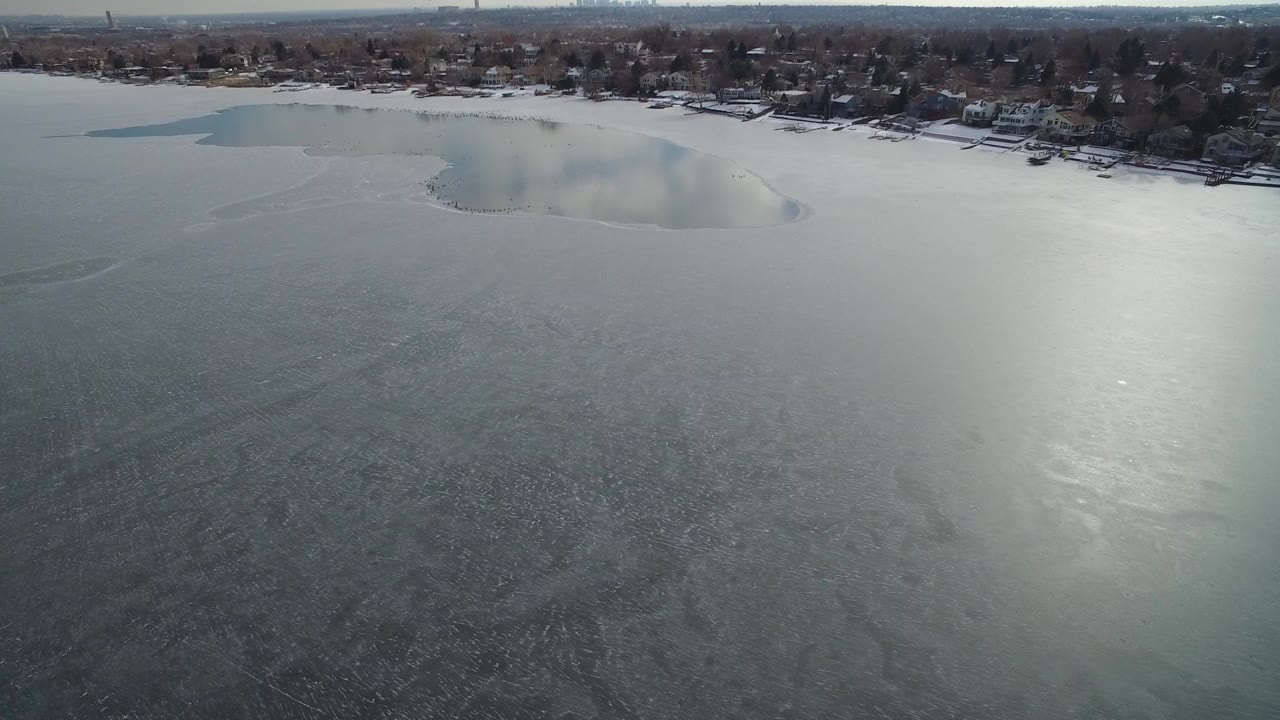 Aerial view over a frozen lake with a residential shoreline.