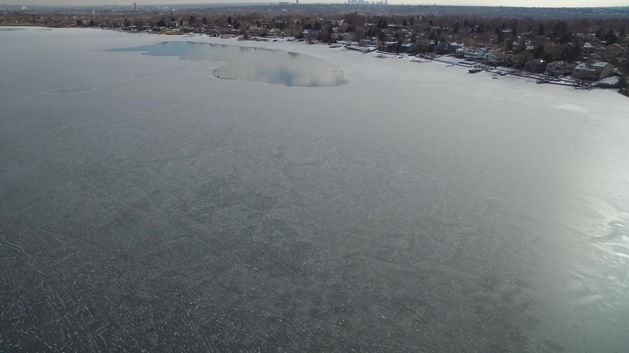 Hidden Lake, Colorado appears from above with textured ice in the foreground, a pale reflection on the water, shoreline houses, and no clearly recognizable people.