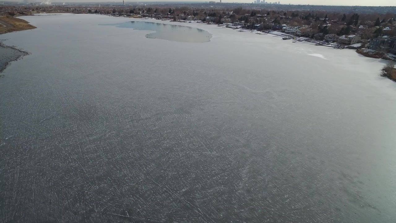 Aerial view over gray lake water toward a residential shoreline