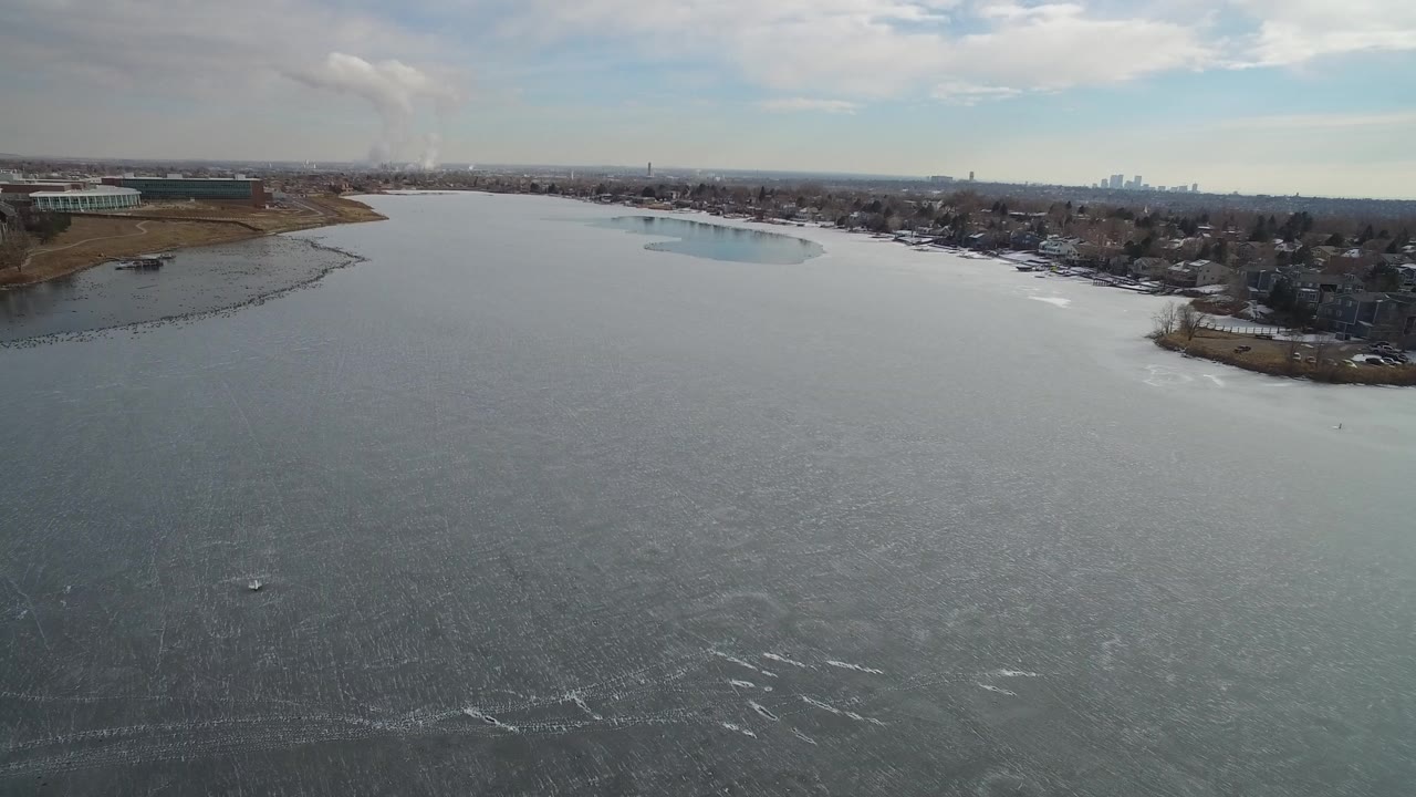 Aerial view over broad water with shoreline homes and distant skyline.