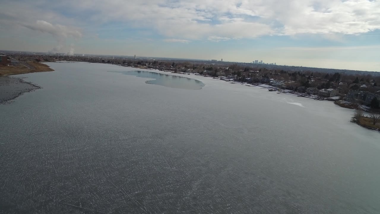 Wide lake aerial with gray rippled water and neighborhood shoreline.