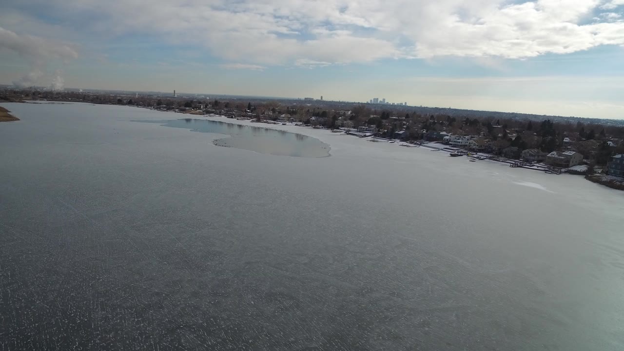 Aerial view over a lake toward a tree-lined shoreline and distant horizon.