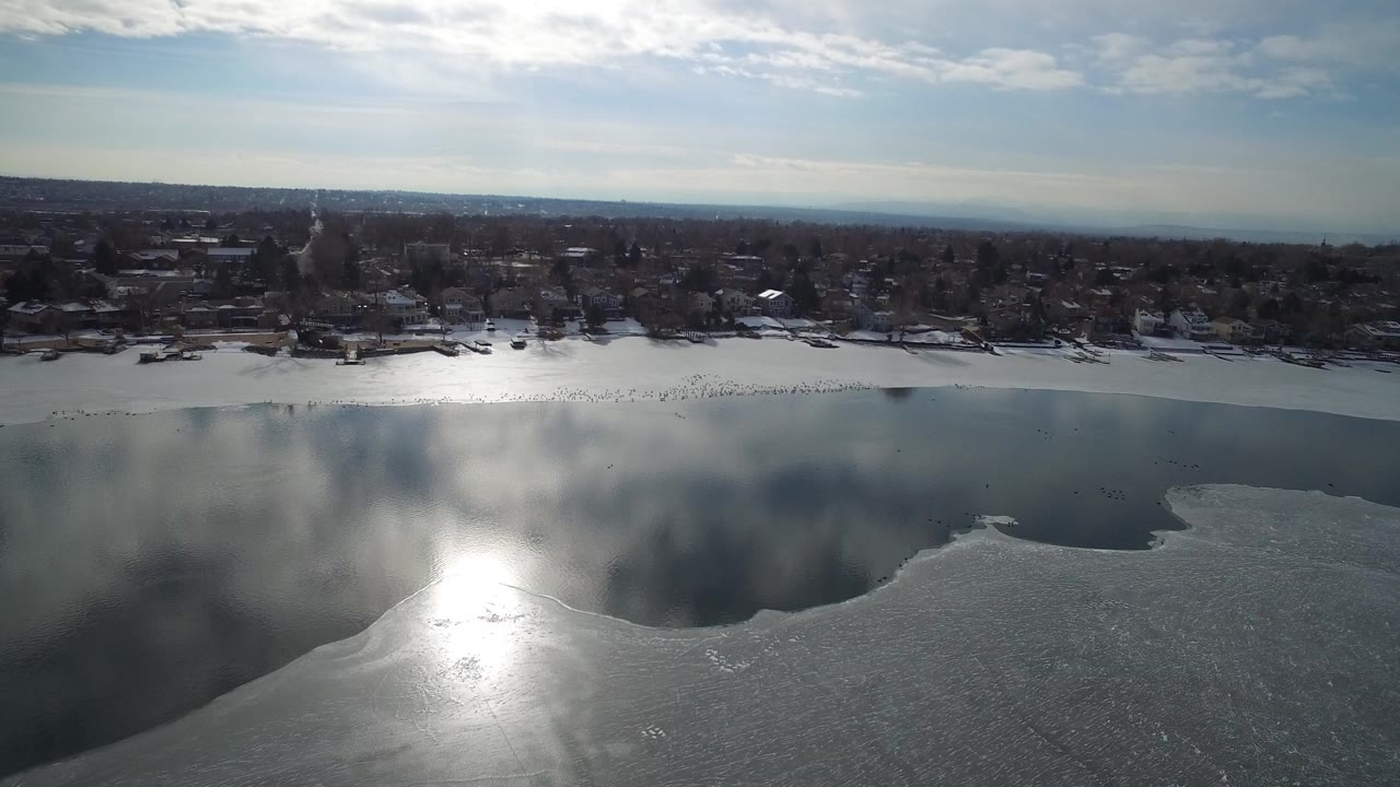 Aerial view of a partially frozen lake beside a winter town shoreline