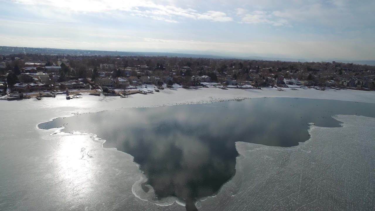 Aerial view of a frozen lake beside snowy residential houses.