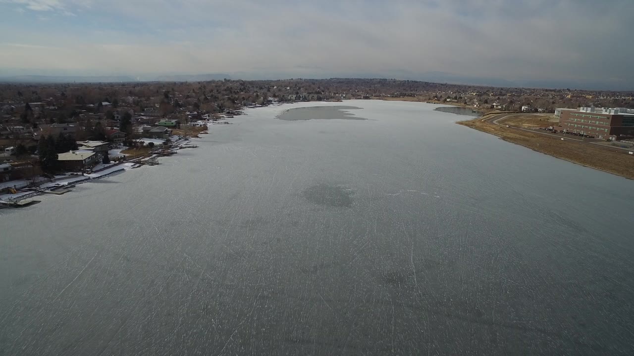Aerial view over gray water toward shoreline homes and large buildings.