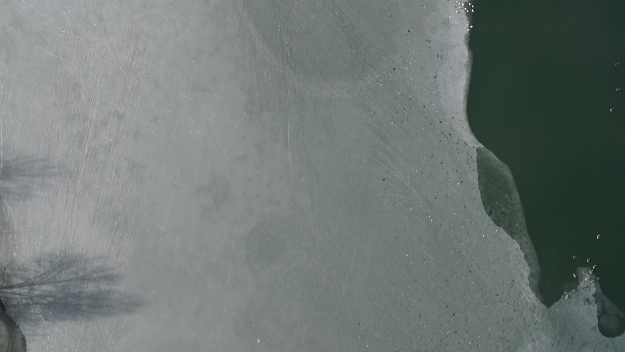 Overhead frozen lake ice with a dark green water opening along the right side.