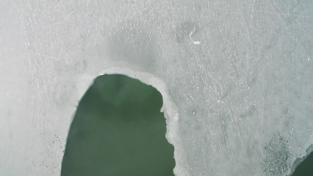 Top-down snowy surface with a dark green lake edge at lower left.