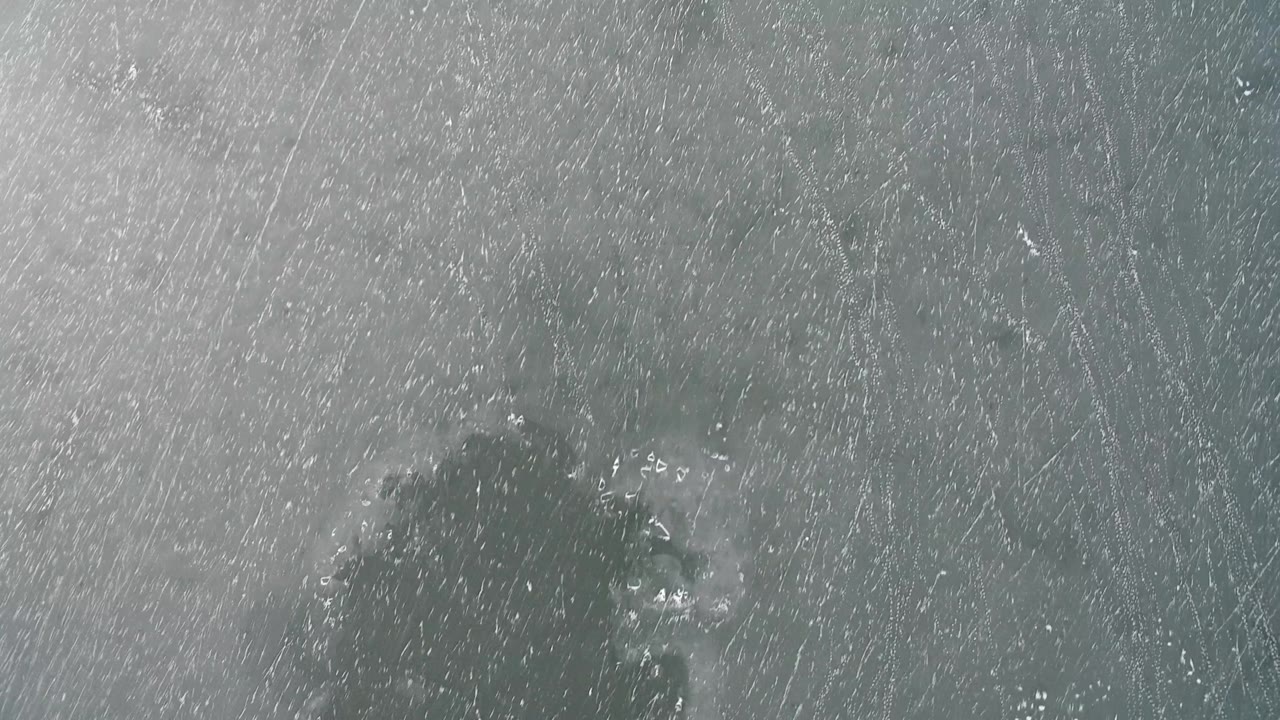 Frozen surface with a dark patch and bright specks on the ice