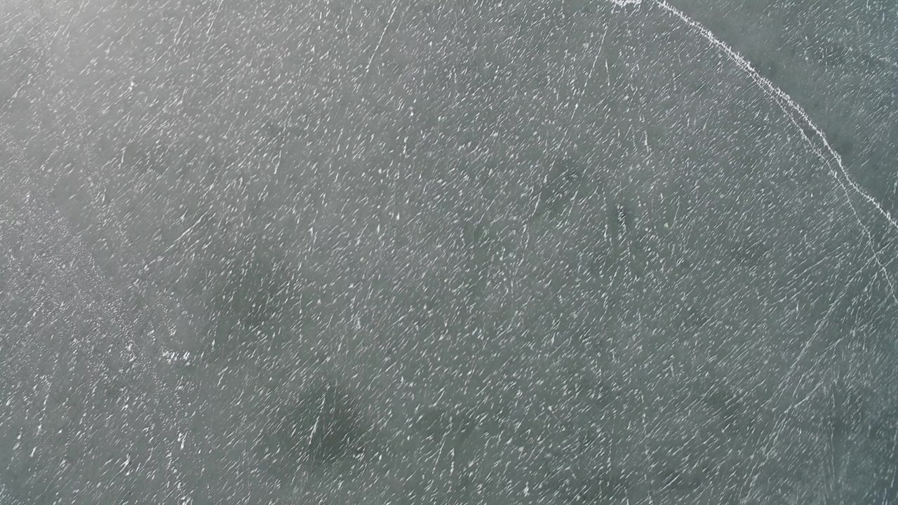 Second overhead frame from Hidden Lake, Colorado with gray-green surface texture and a brighter branching pale line near the upper area, with no visible people.