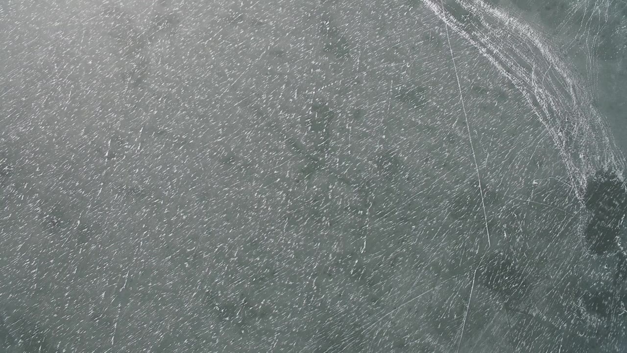 Overhead lake ice with curved bright scrape lines along the upper right.